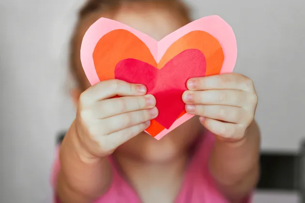 Barn håller utklippta hjärtan i röd, orange, rosa framför sig. Foto: iStock